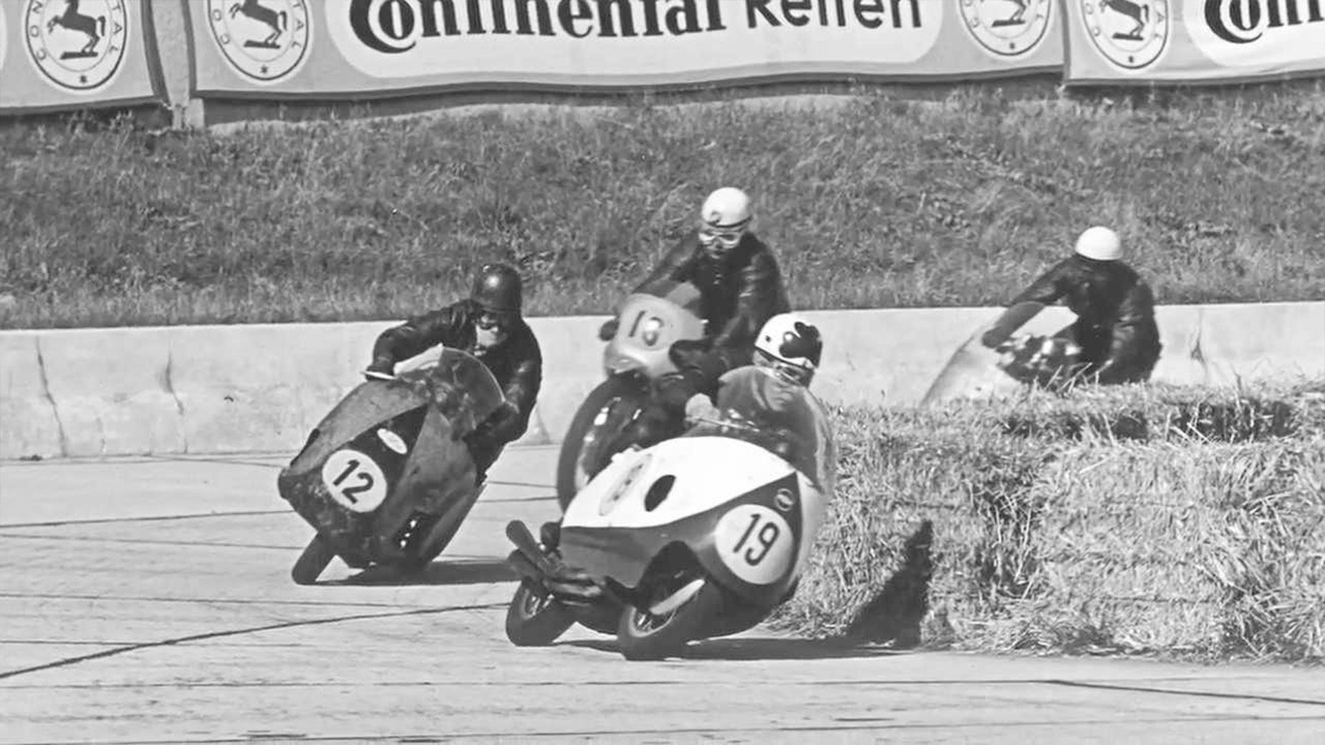 Historic motorcycle road racing action beneath Continental tyre advertising