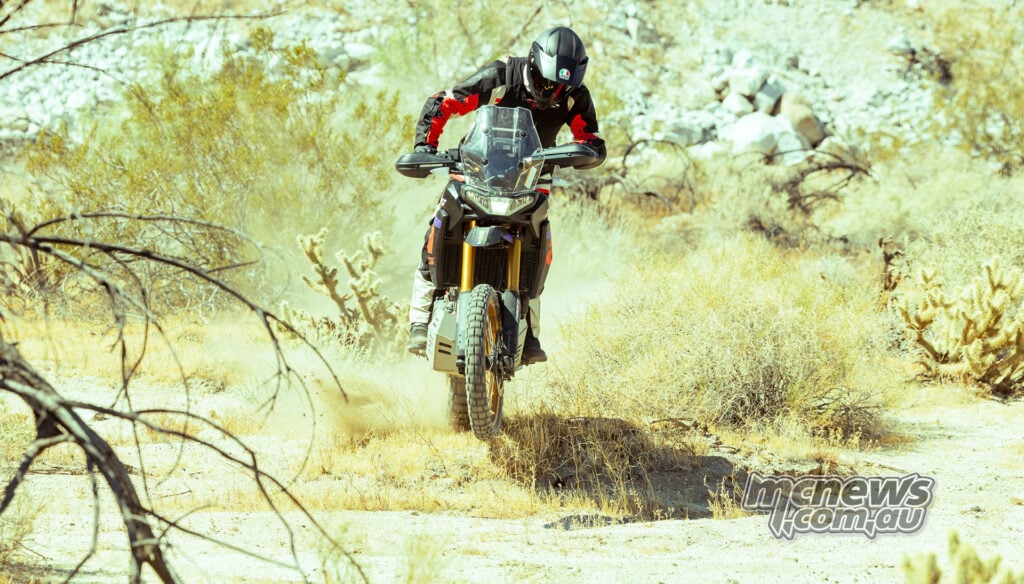 Adventure rider wearing a black Dainese D-air vest while riding an Aprilia Tuareg over a dusty desert trail.