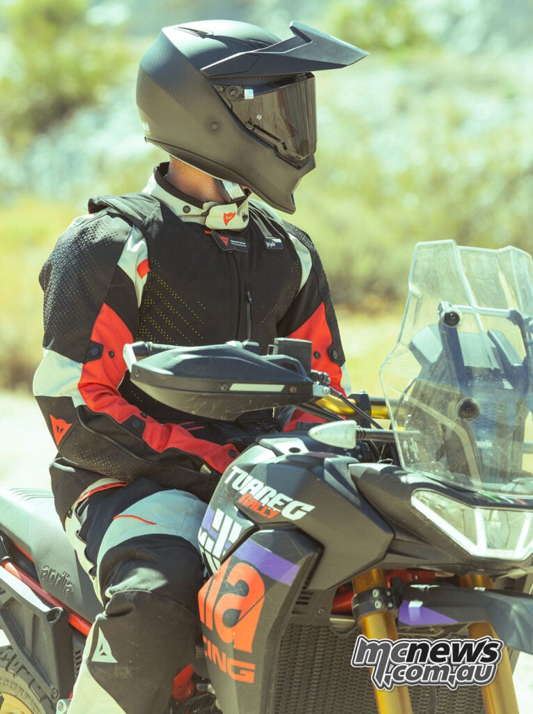 Adventure rider wearing a black Dainese Smart Air vest over a red, white and black motorcycle jacket while seated on an Aprilia Tuareg Rally.