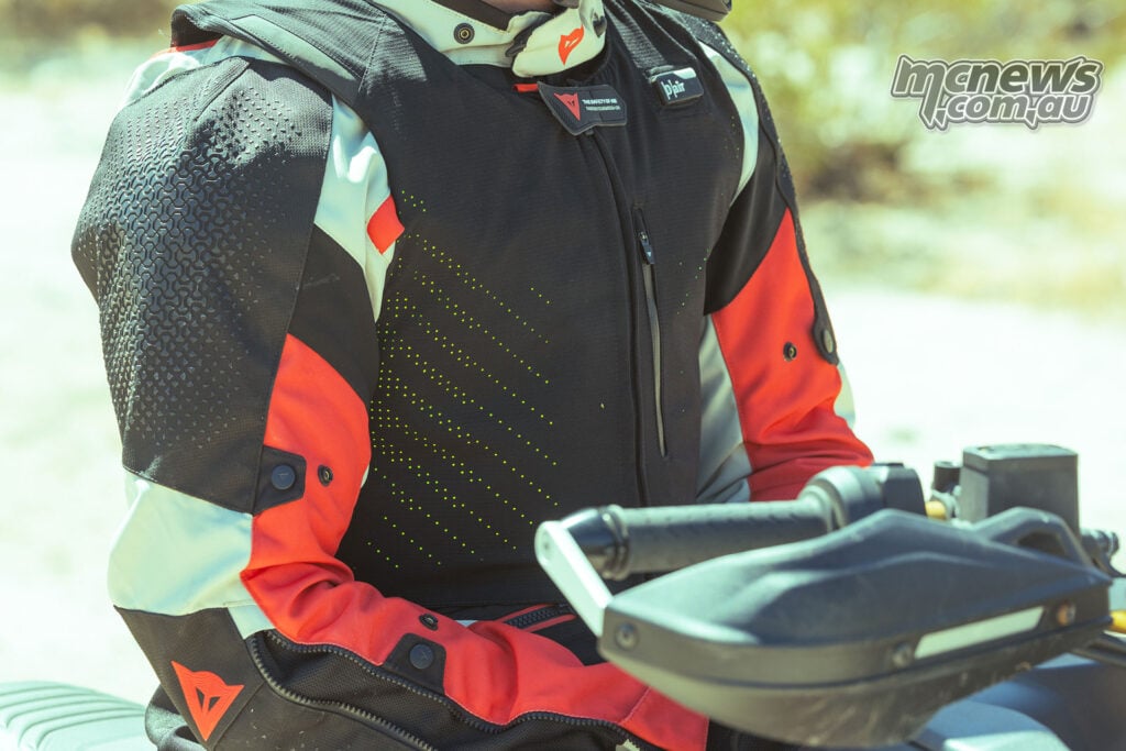 Close-up of a black Dainese Smart Air vest worn over a red, white and black adventure motorcycle jacket, showing the front chest panels and zip.