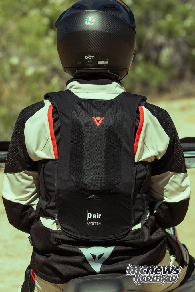 Rear view of an adventure rider wearing a black Dainese Smart Air vest with the D-air System logo visible over a motorcycle jacket.