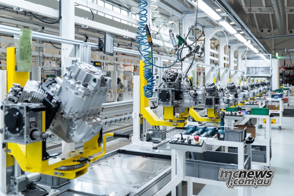 Rows of Moto Guzzi V-twin engines mounted on yellow carriers along the bright factory assembly line.