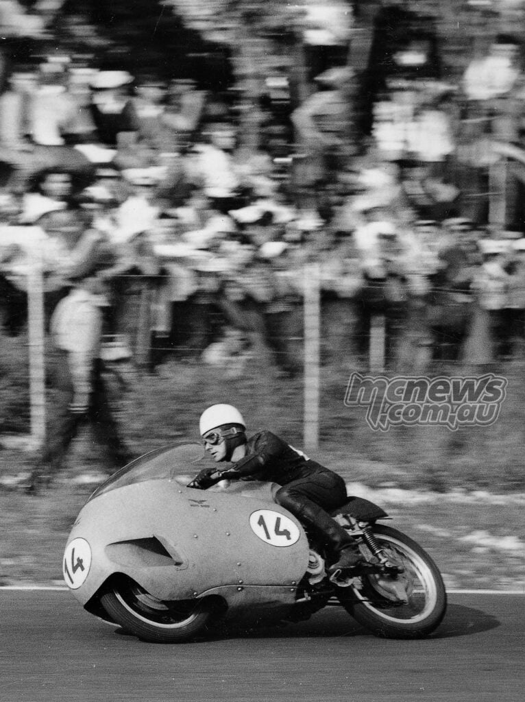 Black-and-white photograph of Keith Campbell racing a streamlined number 14 Moto Guzzi past spectators.