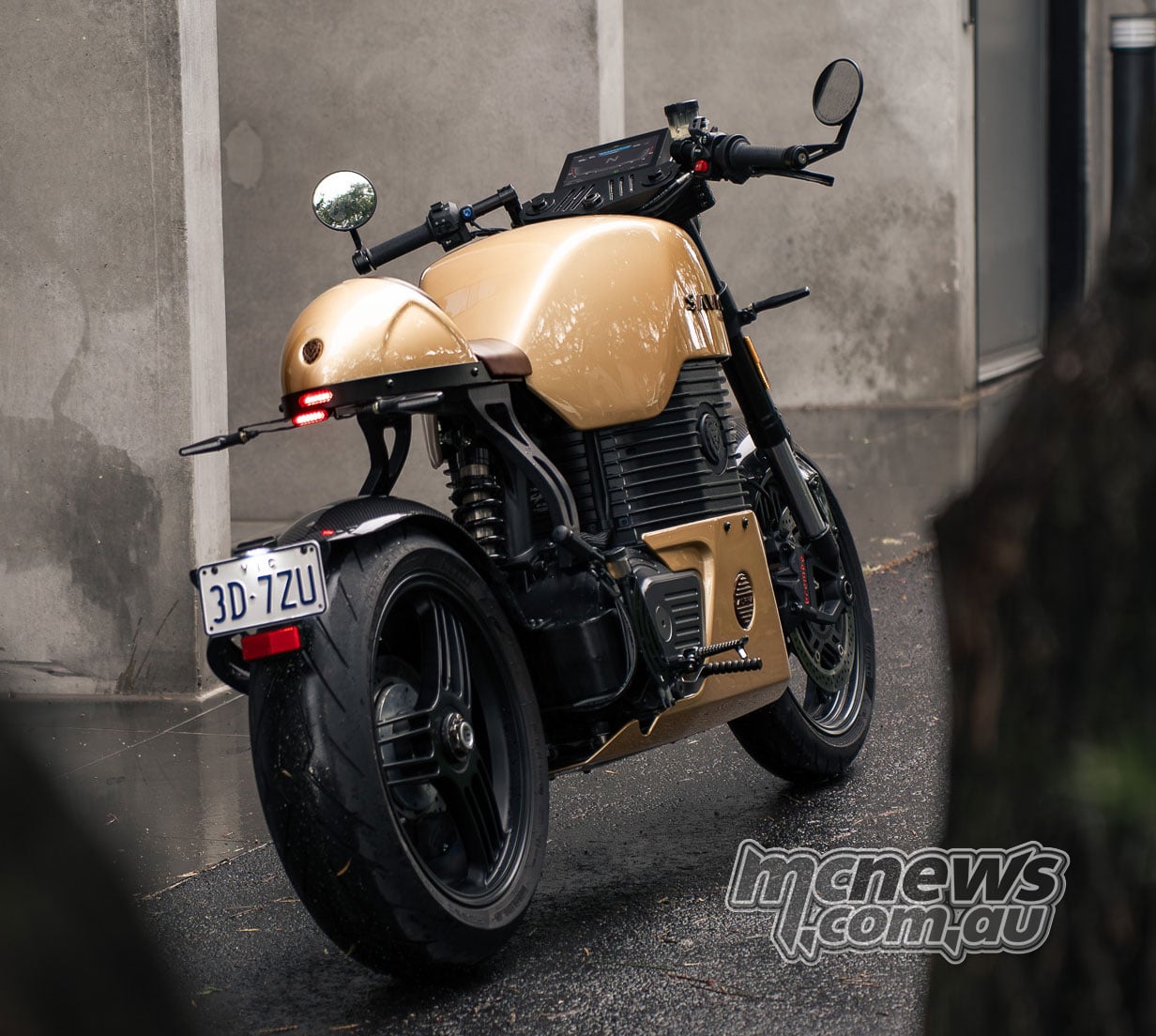 Rear three-quarter view of a gold Savic C-Series electric motorcycle parked in a narrow laneway.