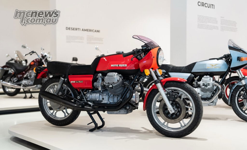 Red Moto Guzzi Le Mans 850 with an exposed V-twin engine and small front fairing on a white museum display.