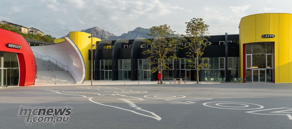 Empty Moto Guzzi courtyard with an eagle graphic on the ground, a yellow café entrance and mountains behind.