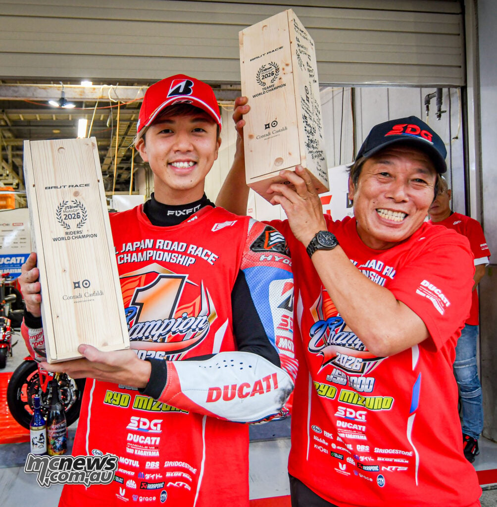Ryo Mizuno and Yukio Kagayama smile while holding wooden presentation boxes in the Ducati garage.