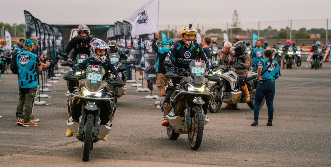 Helmeted riders riding CFMOTO adventure motorcycles through the MT Challenge event staging area.