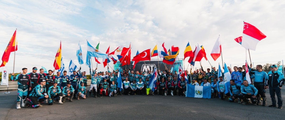 Large group of motorcycle riders and event staff posing together while holding national flags.