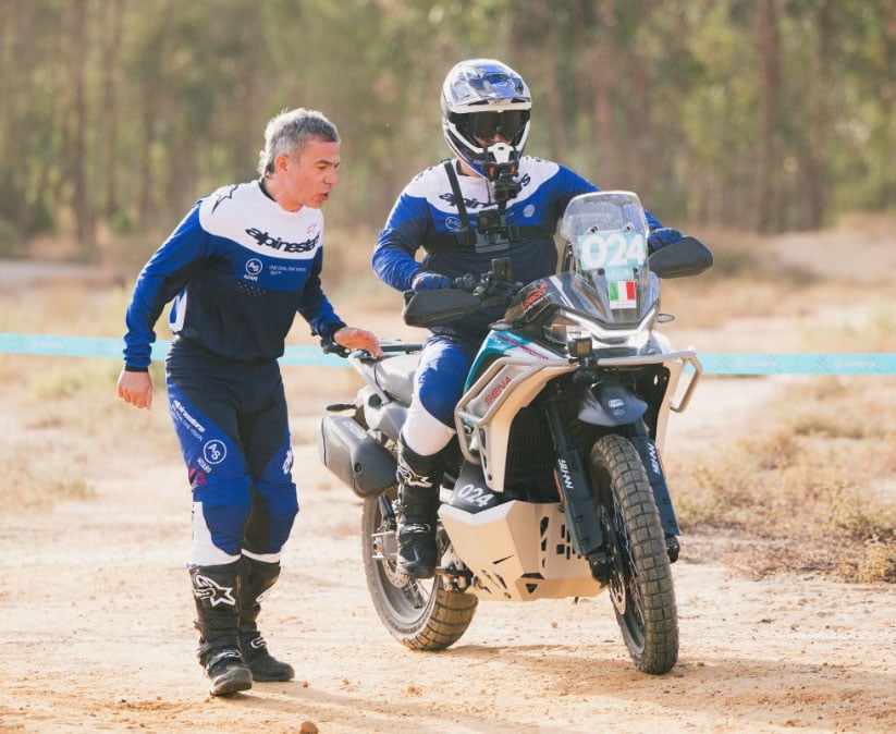 Adventure rider negotiating a slow-speed dirt course while an event official walks alongside the motorcycle.
