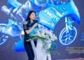 Samantha Liu speaking at the CFMOTO media event in Hangzhou with Grand Prix racing motorcycles projected behind her