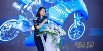 Samantha Liu speaking at the CFMOTO media event in Hangzhou with Grand Prix racing motorcycles projected behind her