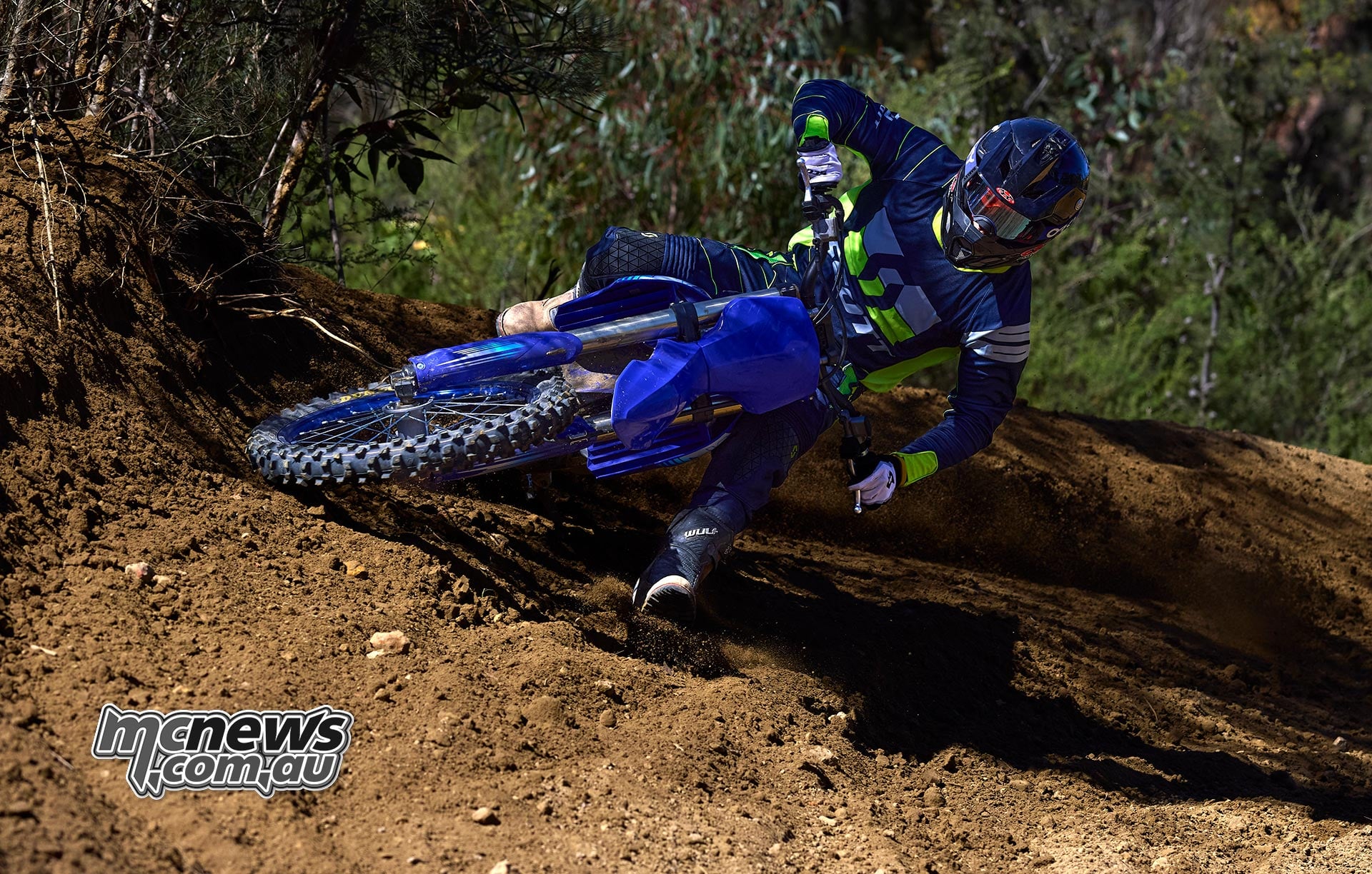Motocross rider leaning a blue Yamaha motorcycle through a deeply rutted dirt berm with the front wheel tracking the rut.