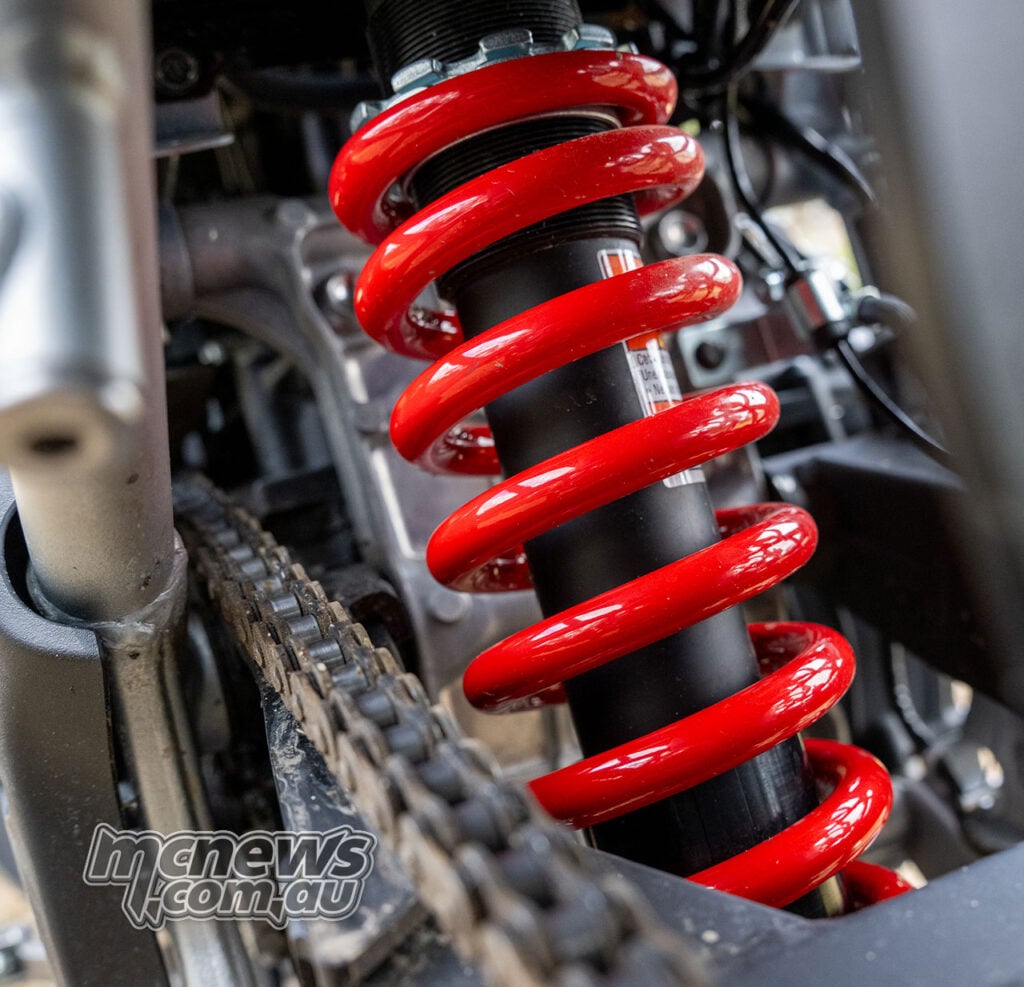 Close-up of the firmer red rear spring fitted around the standard Kawasaki KLE500 SE shock, with its preload collars visible.