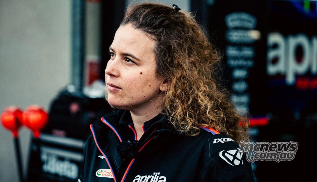 Elena De Cia, Aprilia Racing's Strategy and Data Analysis Lead, pictured in profile wearing Aprilia team clothing in the MotoGP paddock.
