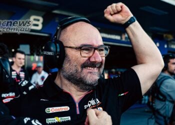 Aprilia Racing technical director Fabiano Sterlacchini smiles broadly and raises a clenched fist in celebration outside the MotoGP garages.