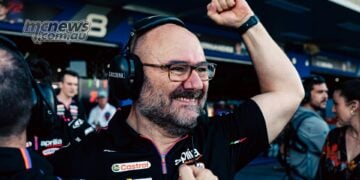 Aprilia Racing technical director Fabiano Sterlacchini smiles broadly and raises a clenched fist in celebration outside the MotoGP garages.