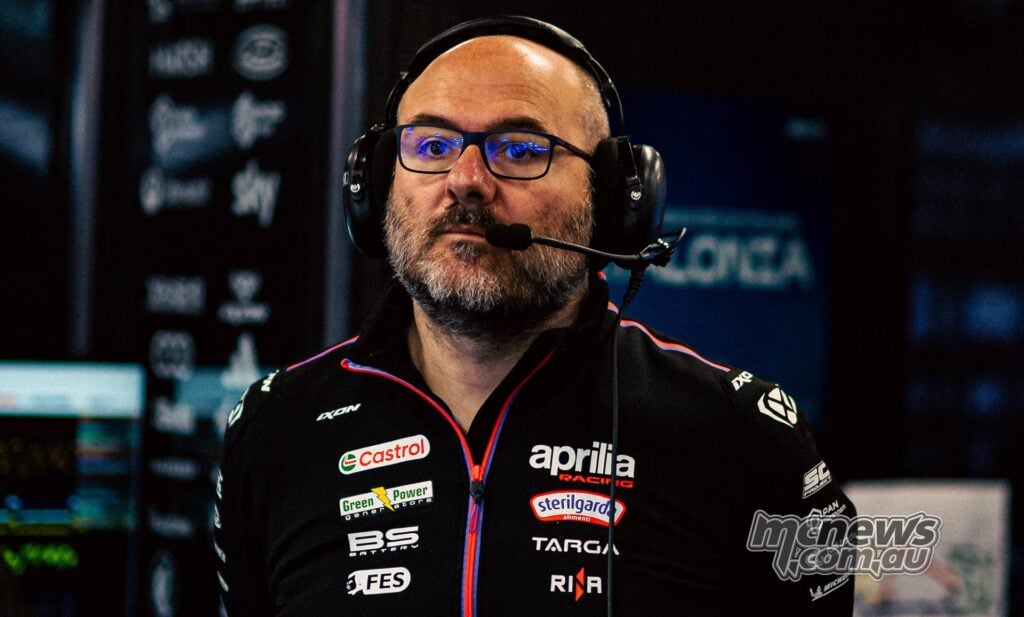 Front-facing portrait of Aprilia MotoGP technical director Fabiano Sterlacchini wearing blue-framed glasses, a communications headset and black Aprilia Racing team clothing.