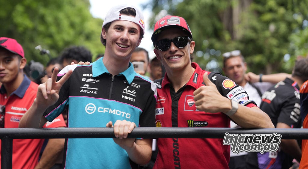 Maximo Quiles makes a peace sign beside Marc Marquez, who gives a thumbs-up at the Mandalika parade.
