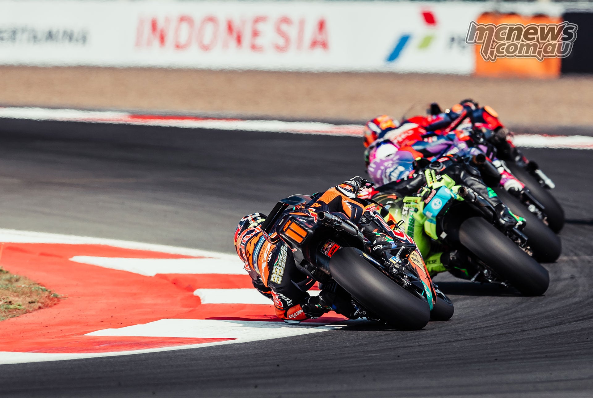 Brad Binder leads a line of riders through a right-hand bend, viewed from behind.