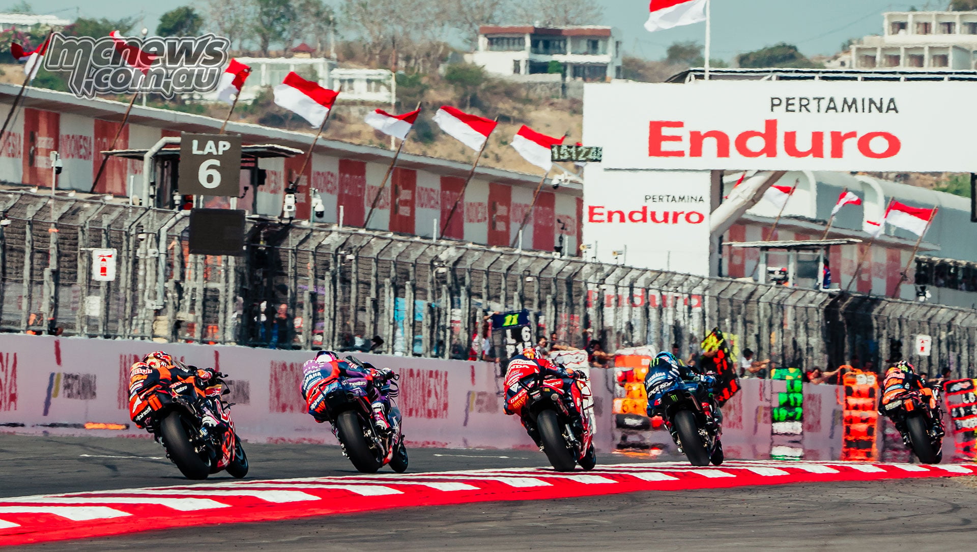 Riders accelerate along the Mandalika pit straight past pit boards and Indonesian flags.