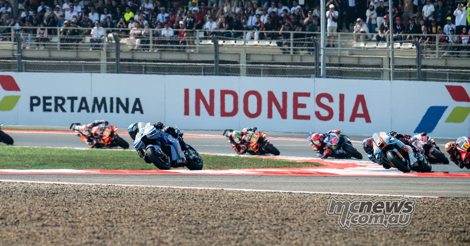 Alex Marquez and Ai Ogura among a group of riders cornering in front of the Mandalika grandstand