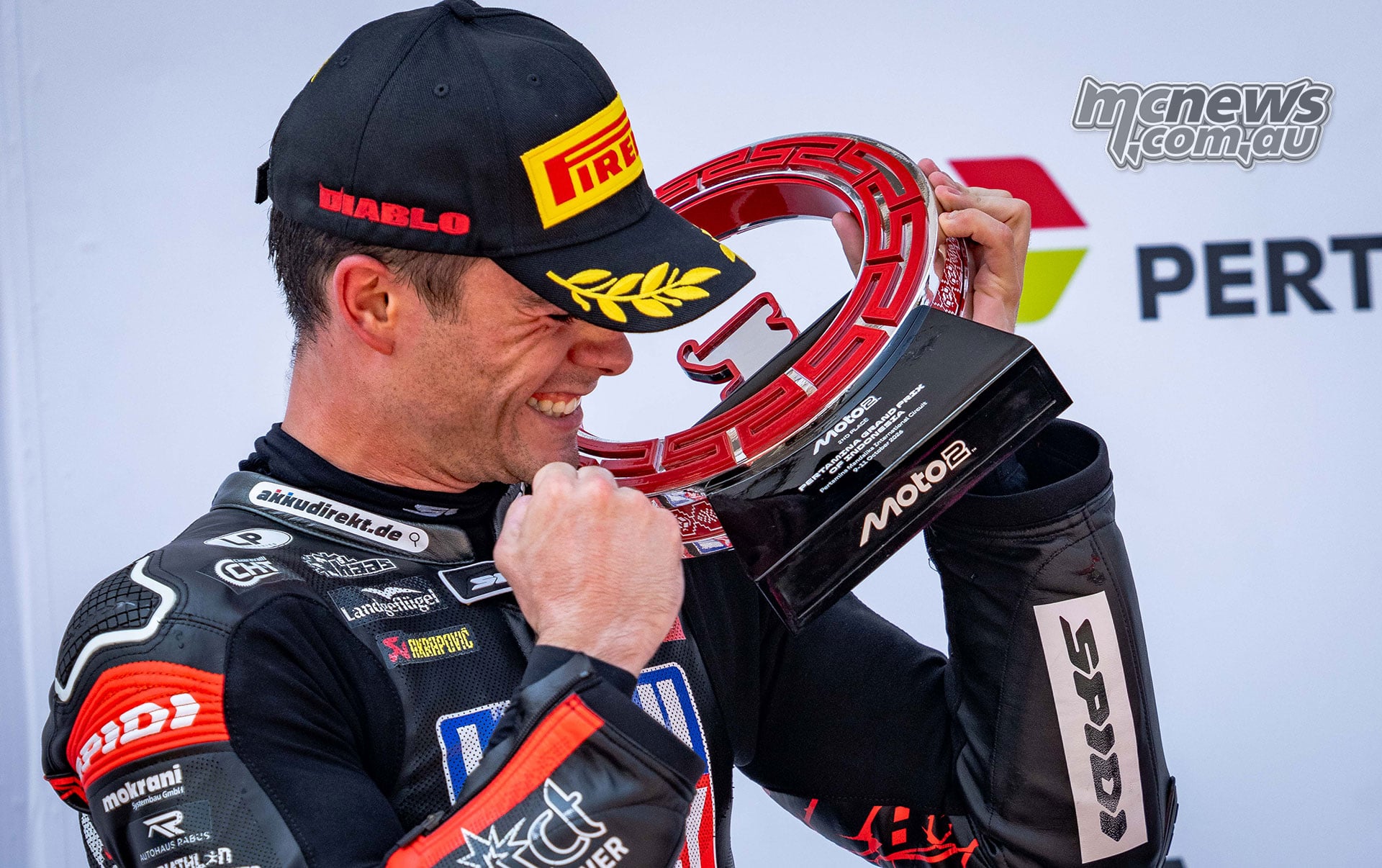 Manuel Gonzalez smiles while holding his second-place Moto2 trophy against his shoulder.