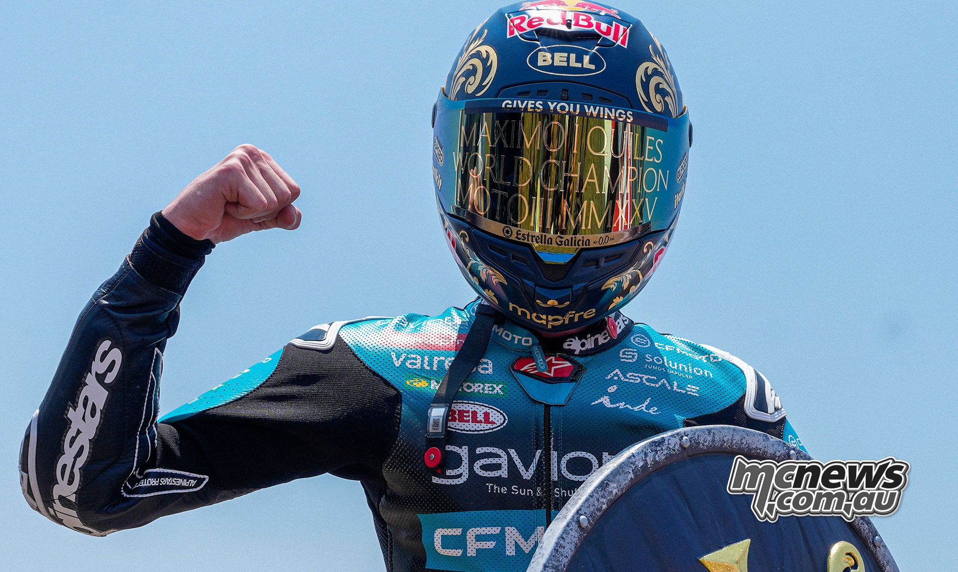 Maximo Quiles raises his fist while wearing a gold-lettered world champion visor and holding a championship shield.