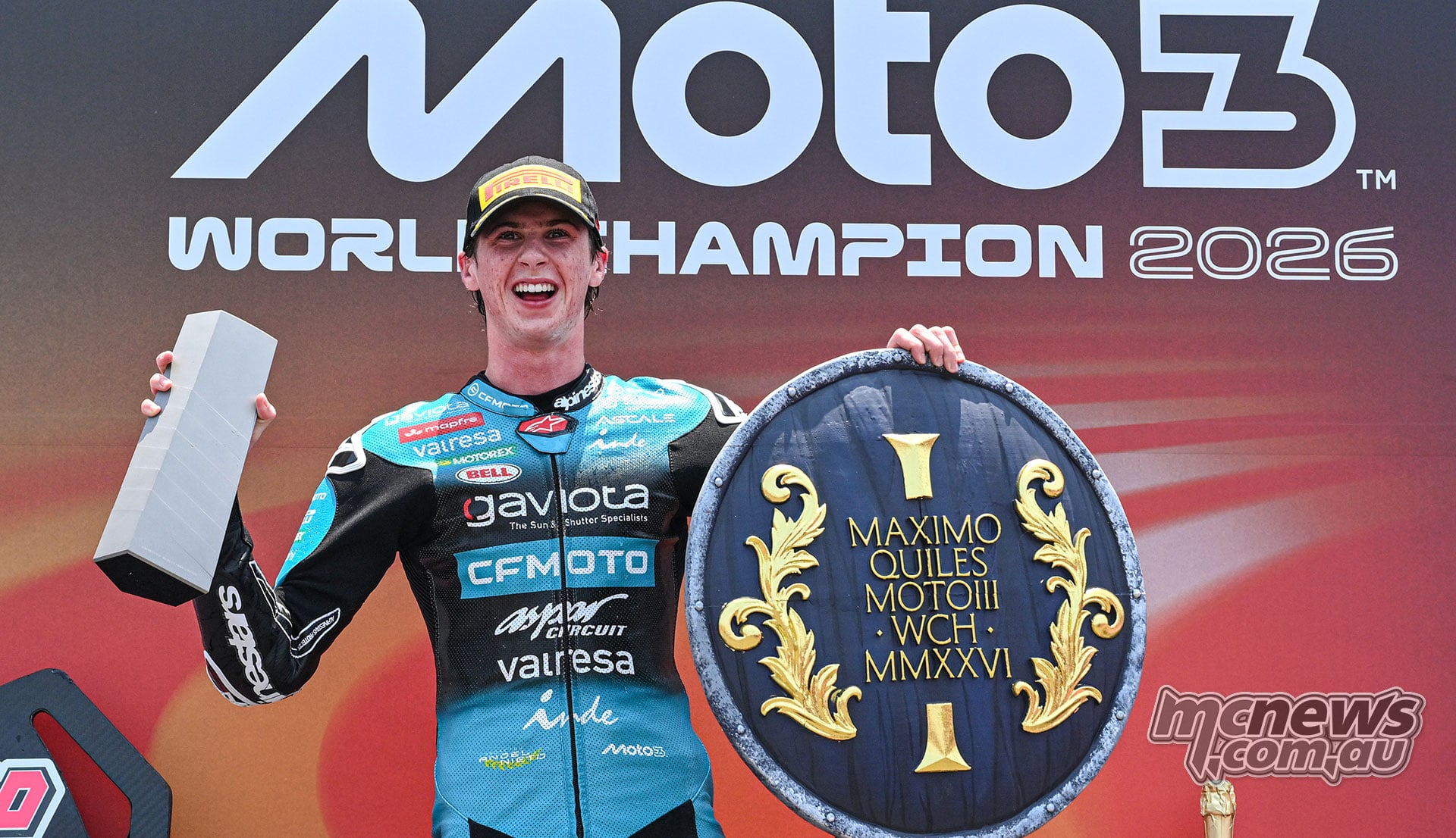 Maximo Quiles smiles while holding a silver number-one trophy and a blue and gold championship shield.