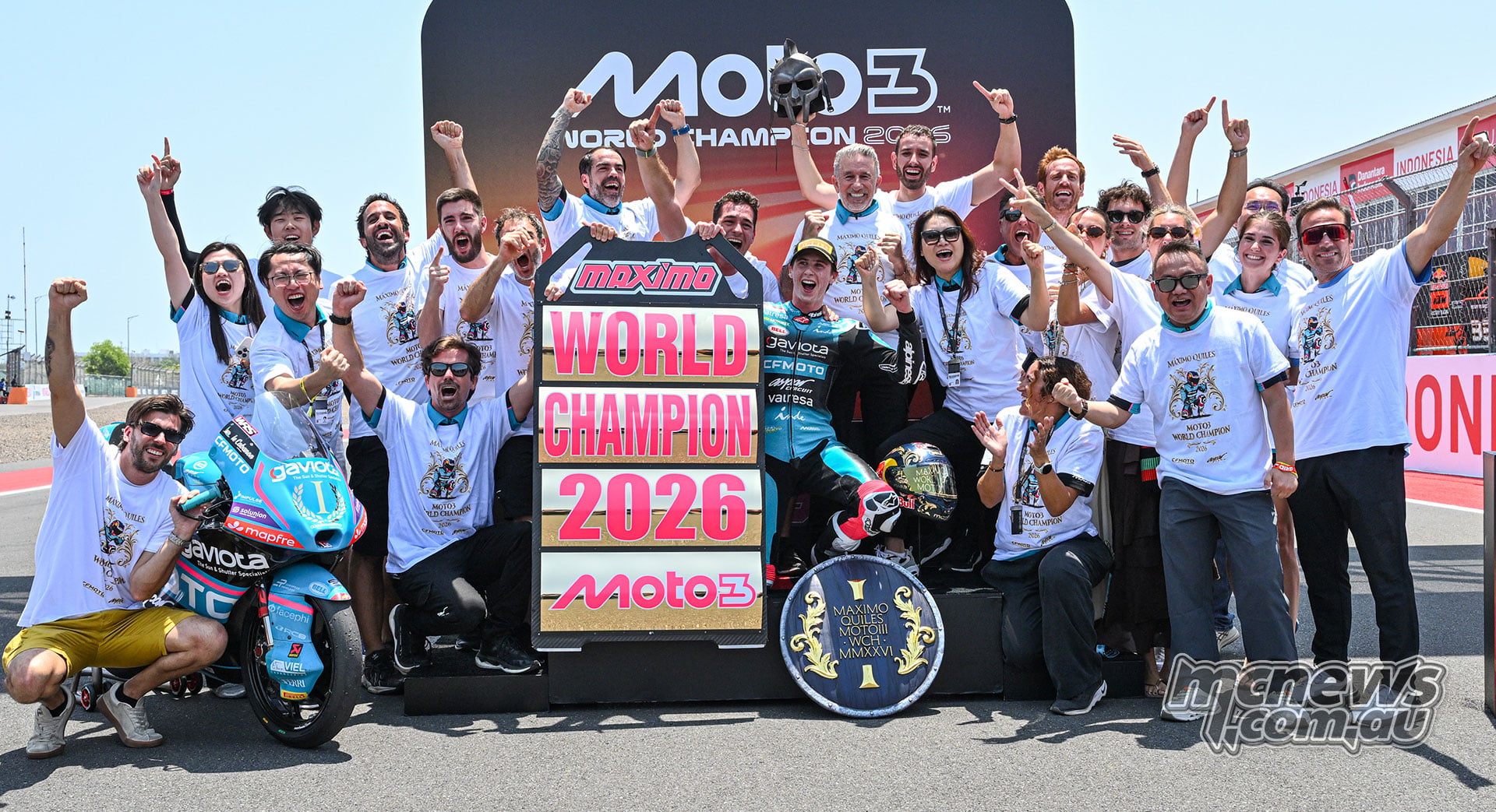 Maximo Quiles celebrates with his team and supporters around his motorcycle and world champion board.