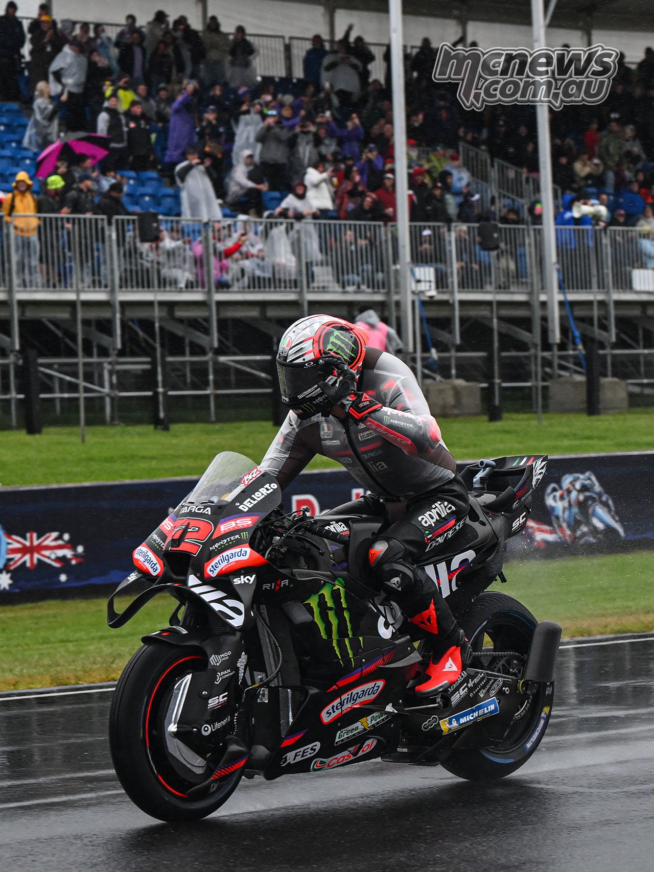 Marco Bezzecchi rides his black number 72 Aprilia on the wet Phillip Island main straight in front of the grandstand.