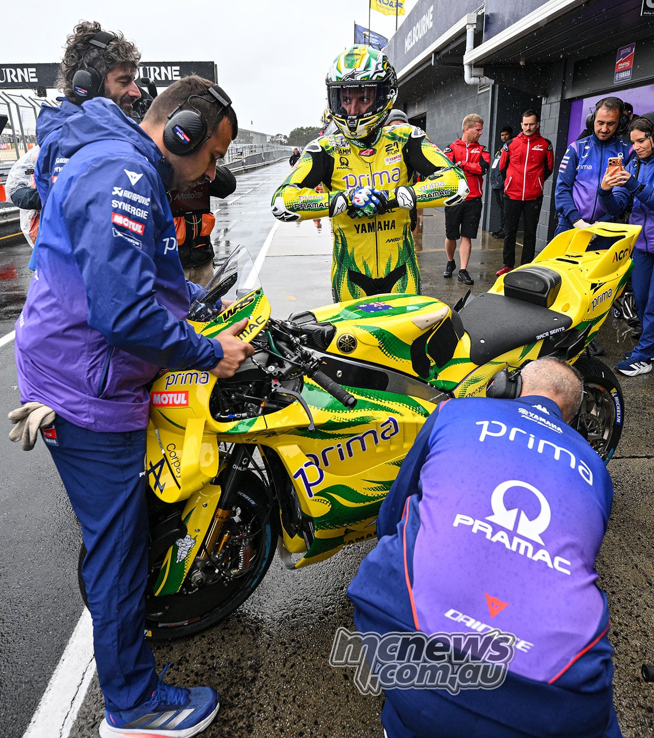 Jack Miller stands behind his green-and-yellow Pramac Yamaha as crew members work around the motorcycle in pit lane.