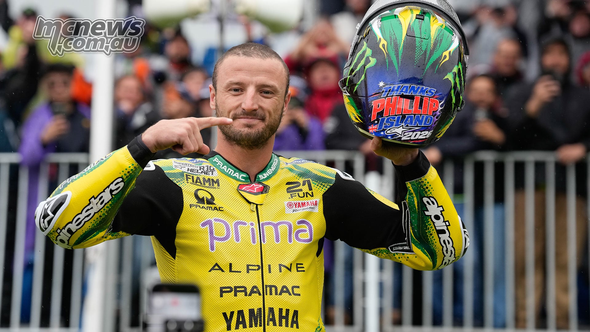 Jack Miller holds up his green-and-yellow helmet and points to its Thanks Phillip Island 2026 message in front of spectators.