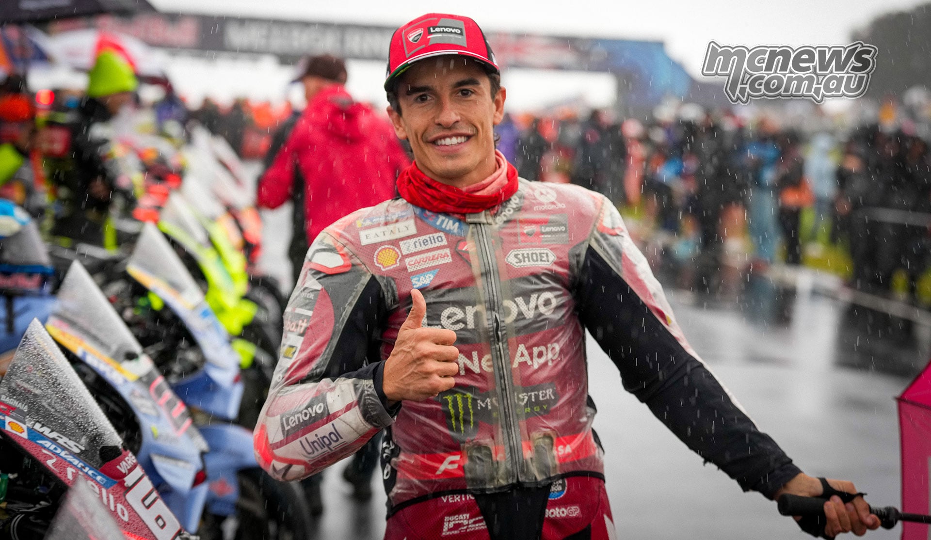 Marc Marquez gives a thumbs-up in Ducati leathers and a clear rain jacket on the wet grid.