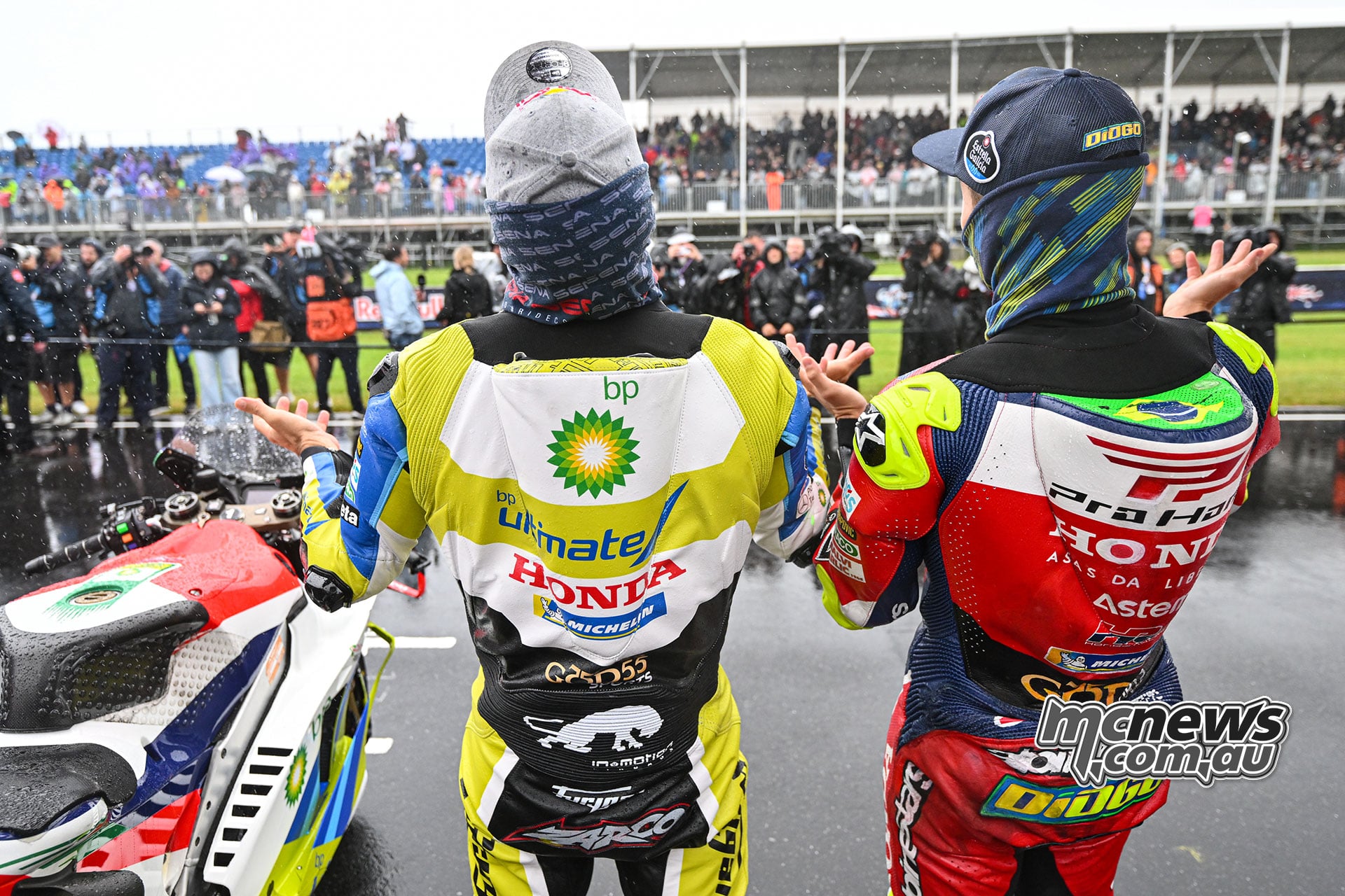 Viewed from behind, Johann Zarco and Diogo Moreira raise their hands towards the spectators while standing beside a Honda.