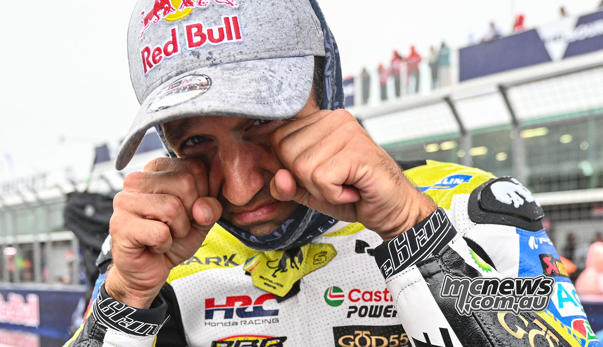 Johann Zarco presses his fists beneath his eyes while looking at the camera in Honda leathers and a grey Red Bull cap.