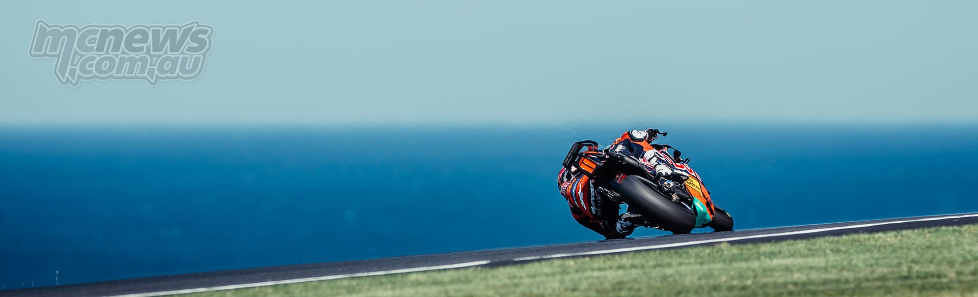 Rear view of Pedro Acosta leaning his KTM into a Phillip Island corner with the blue sea beyond.