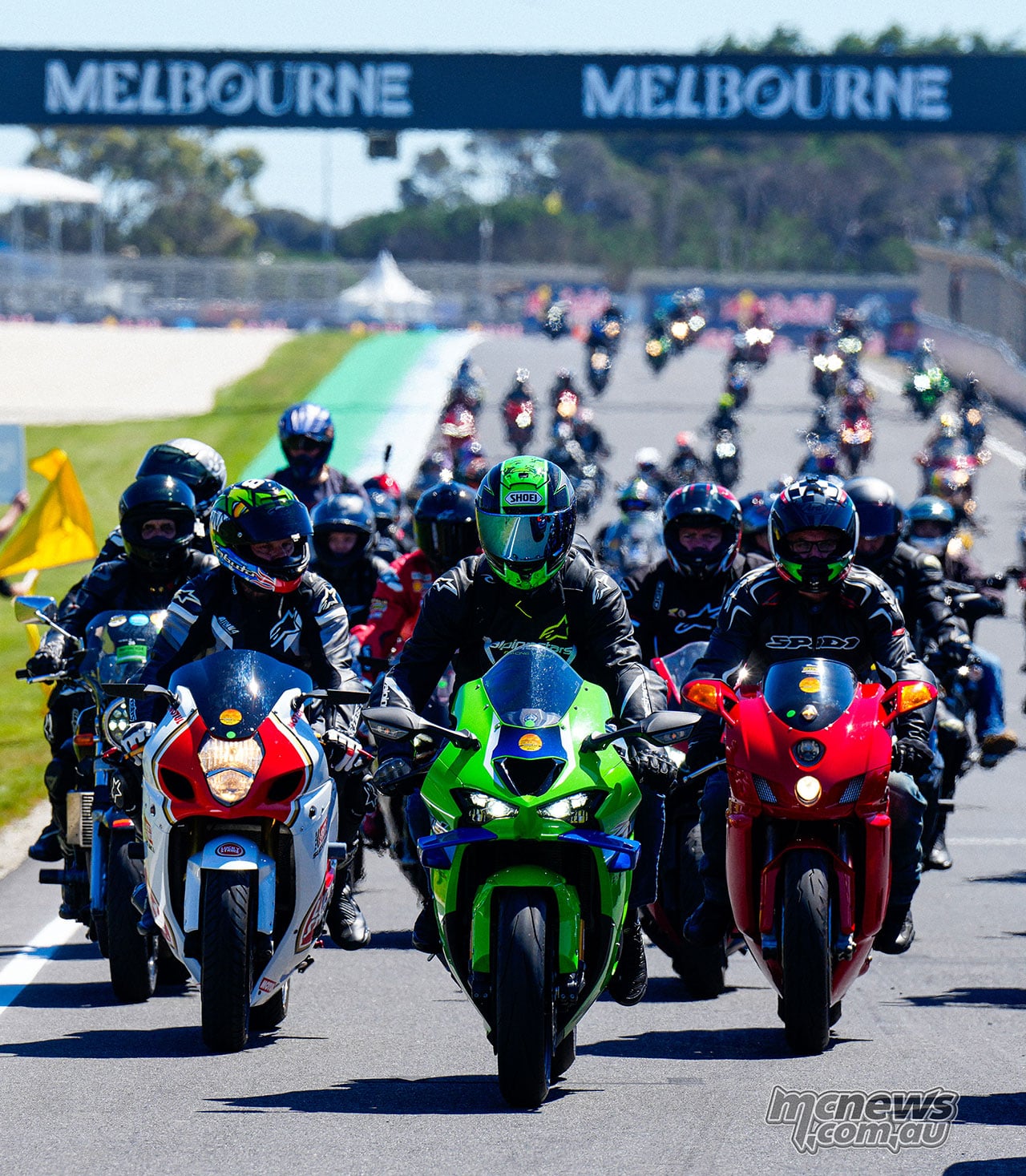 Road riders on sports bikes lead a long line of motorcycles along Gardner Straight beneath the Melbourne bridge.