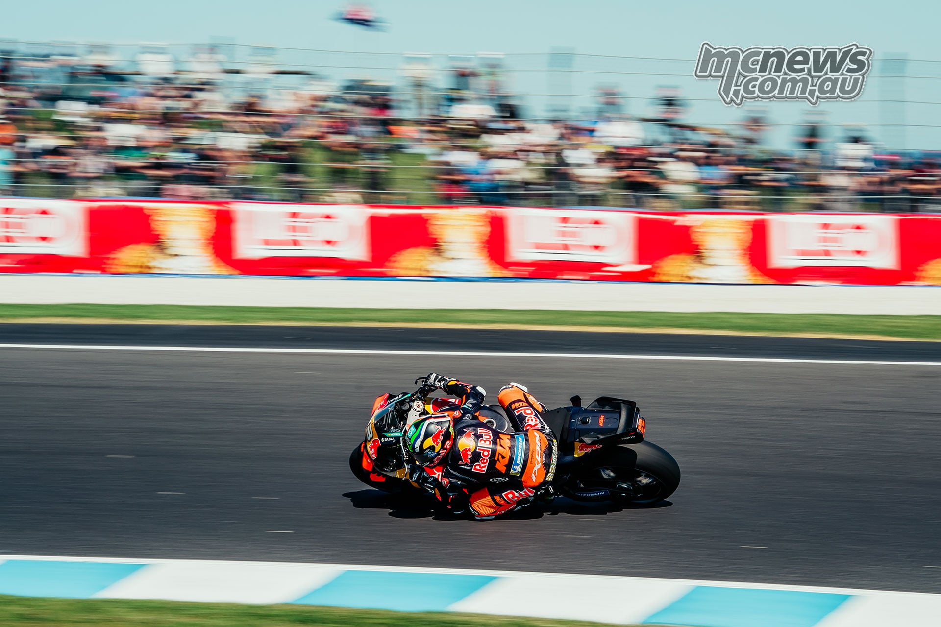 Brad Binder leans his orange KTM through a Phillip Island corner with spectators behind the fencing.