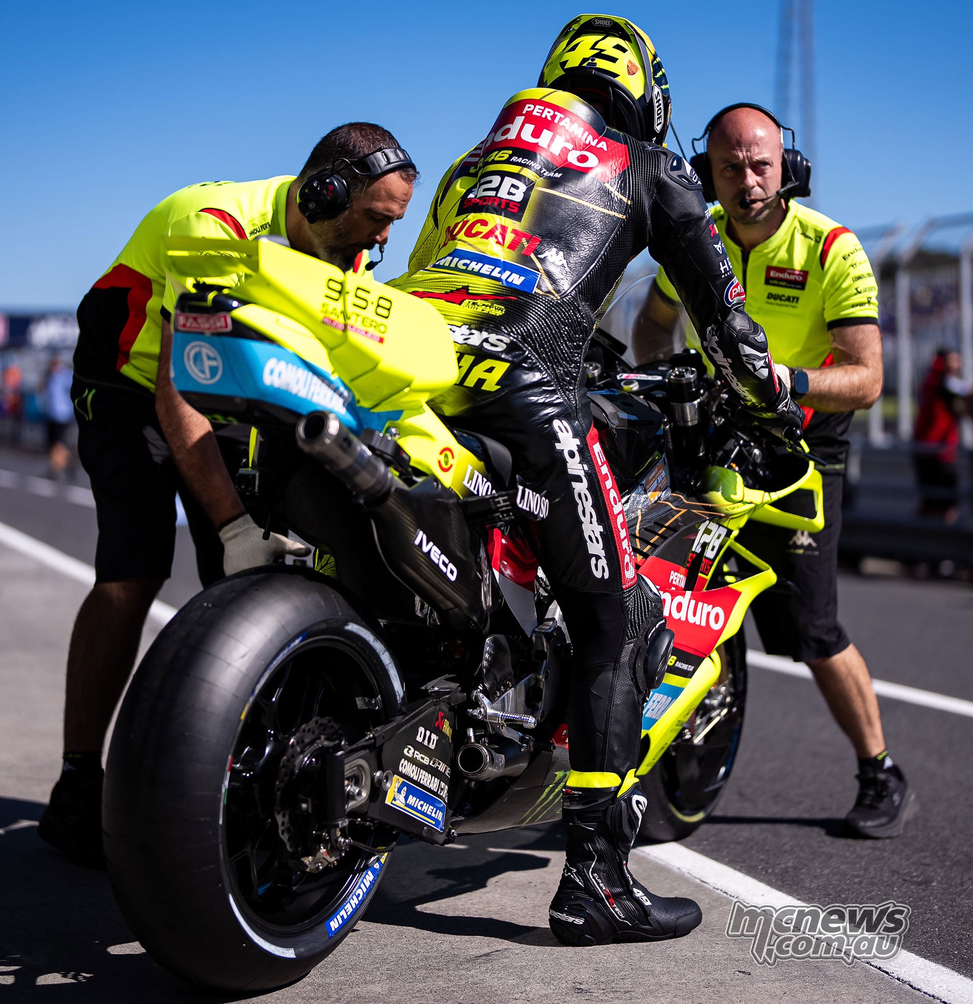 Fabio Di Giannantonio sits on his yellow VR46 Ducati in pit lane while two crew members work around the bike.