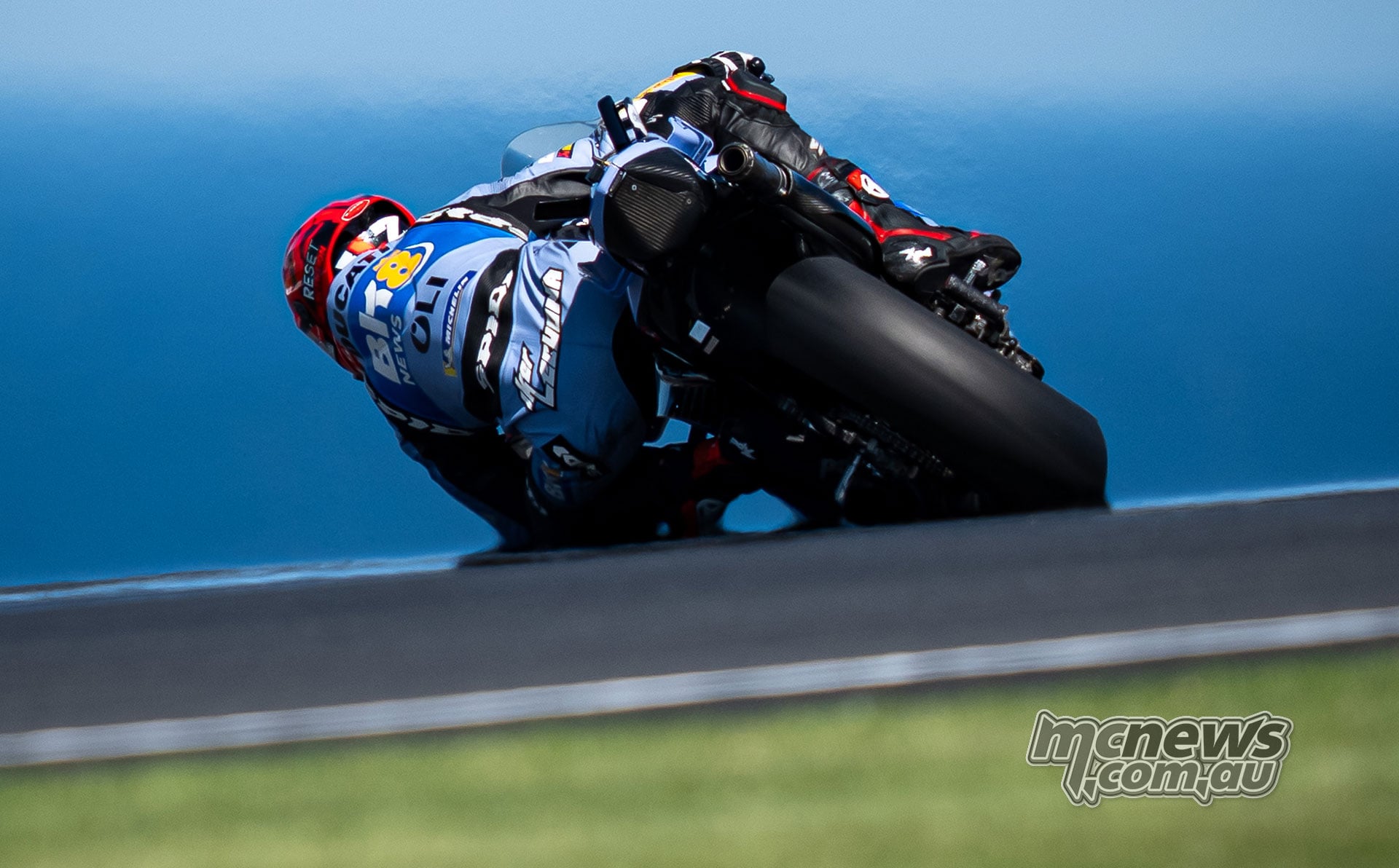 Rear view of Iker Lecuona leaning his blue Gresini Ducati through a corner with the sea behind him.