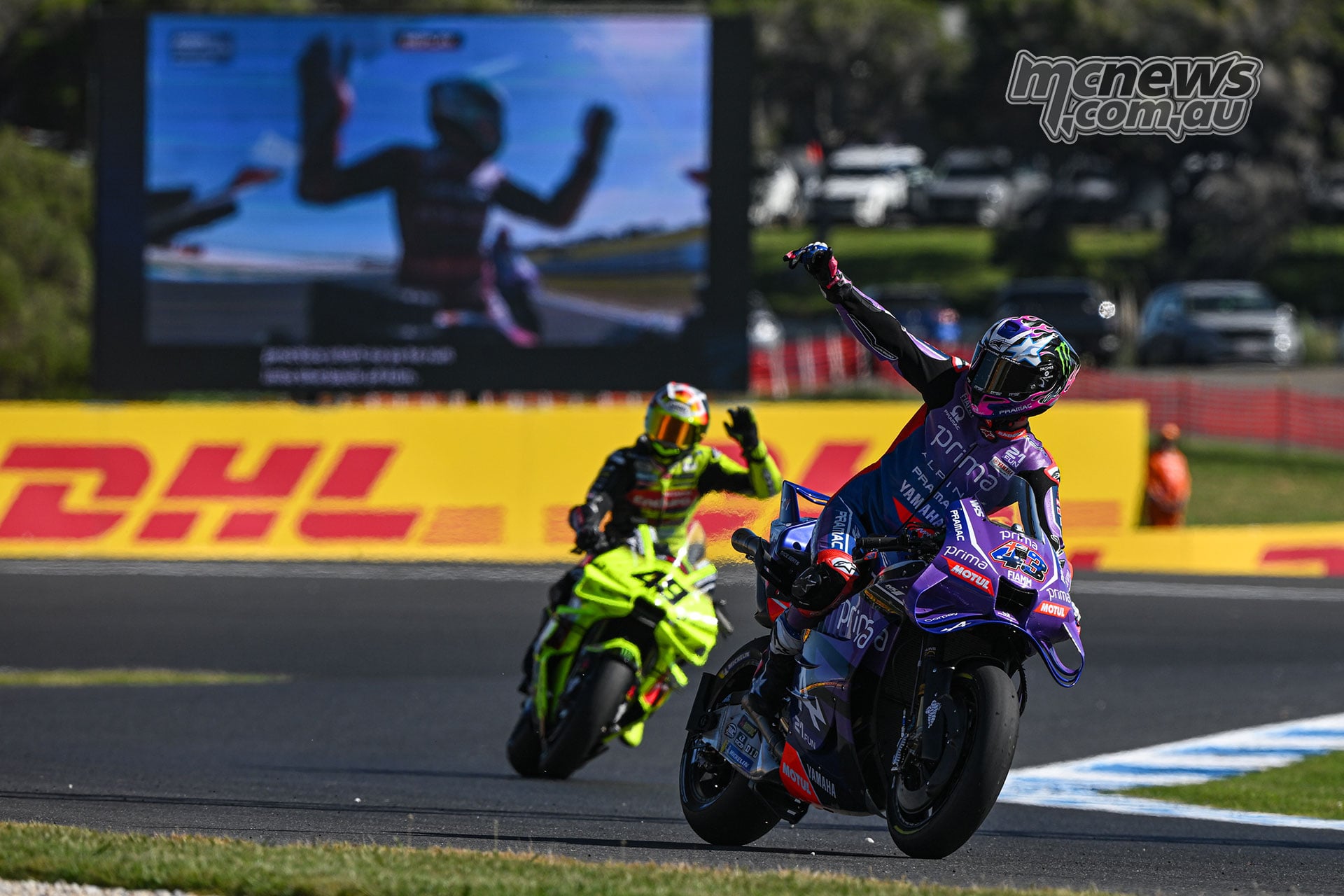 Jack Miller raises an arm on his purple Pramac Yamaha with Fabio Di Giannantonio following on a yellow Ducati.