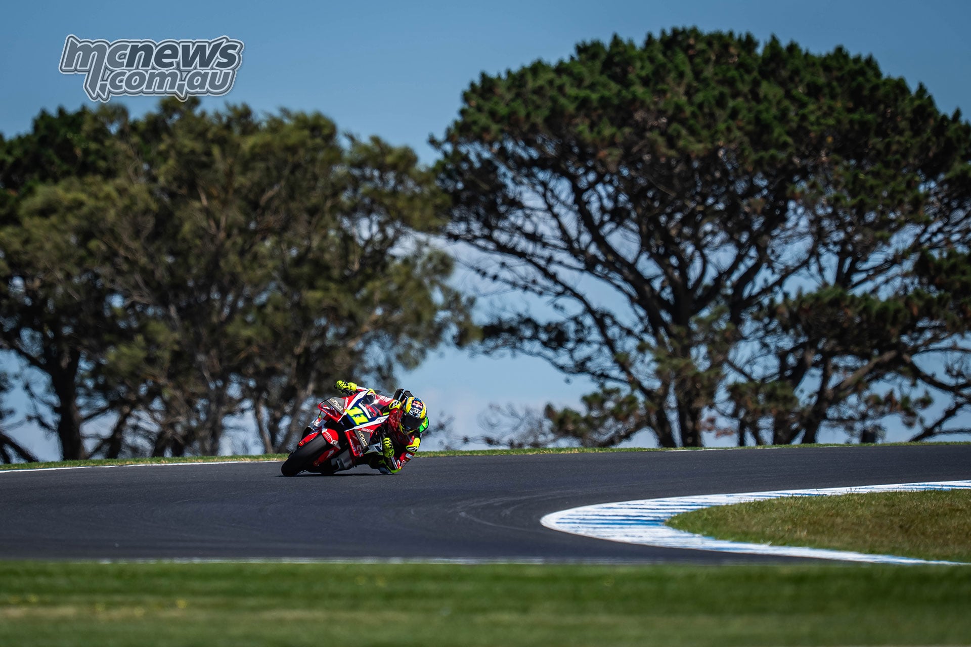 Diogo Moreira rides his red, white and yellow LCR Honda over a rise at Phillip Island, with trees behind.