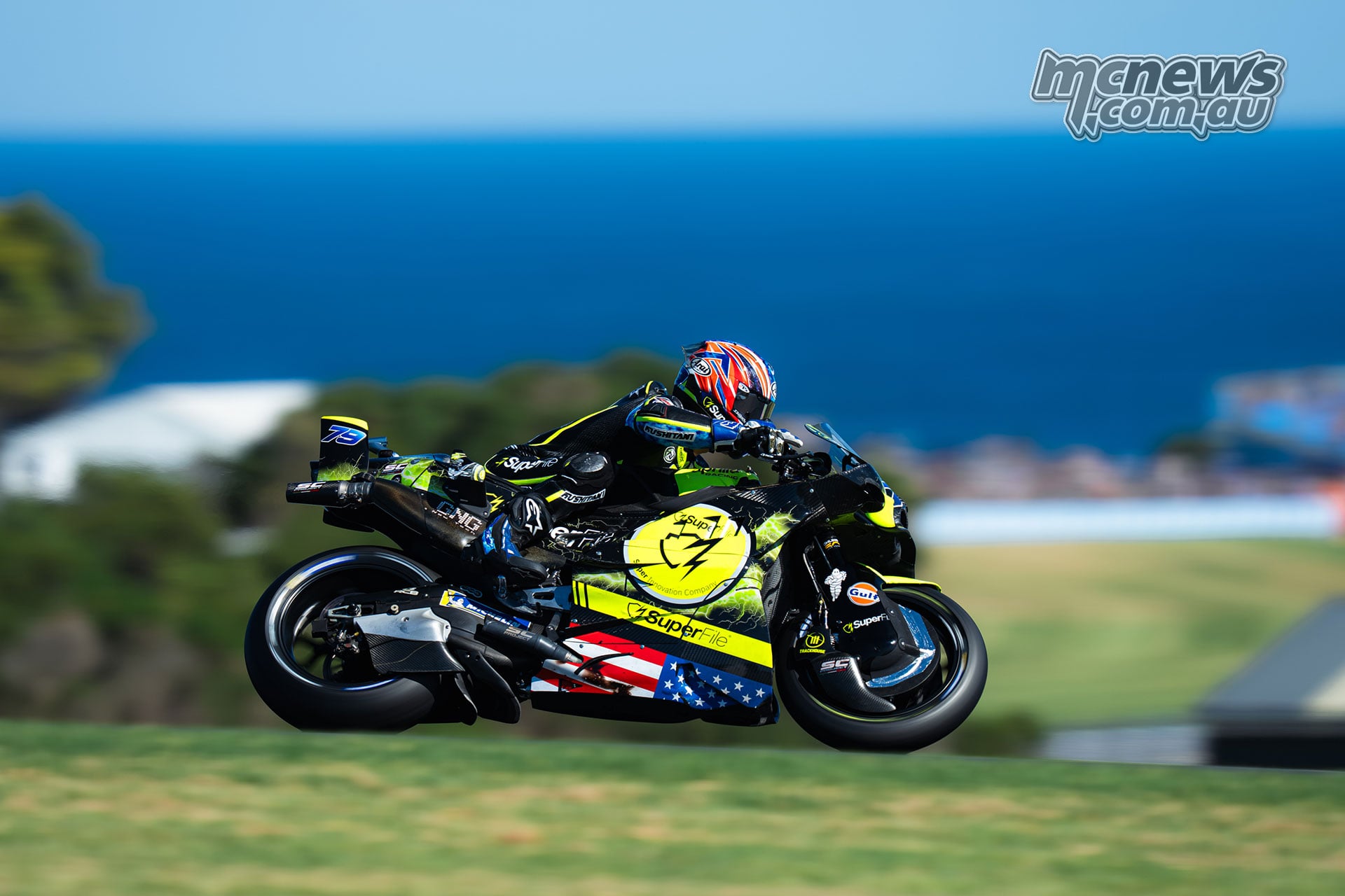 Ai Ogura corners on the yellow and black Trackhouse Aprilia with the sea behind him.