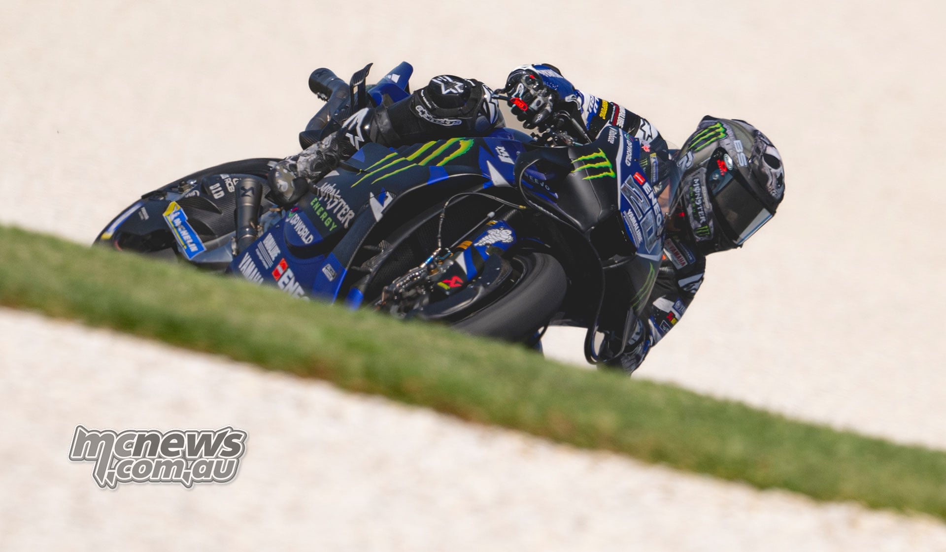 Fabio Quartararo leans his Yamaha into a corner, partially obscured by a grassy bank.