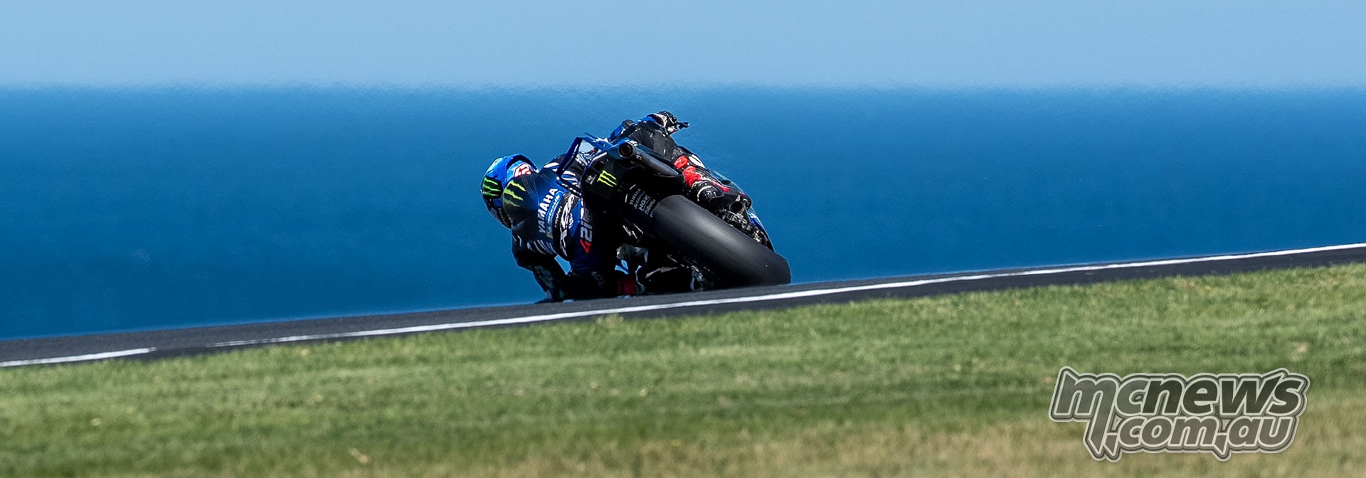 Rear view of Alex Rins leaning his Yamaha into a corner with the blue sea beyond the circuit.