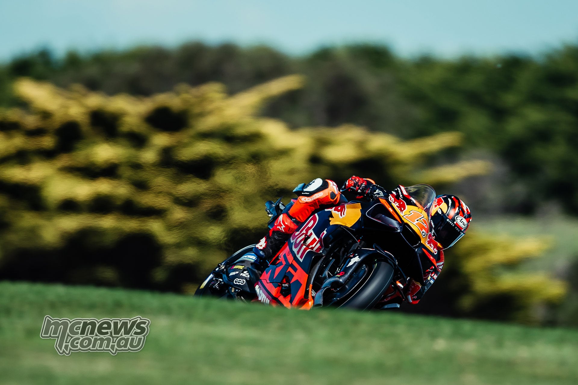 Maverick Vinales rides his orange number 12 Red Bull KTM Tech3 bike through a corner behind a grassy foreground.