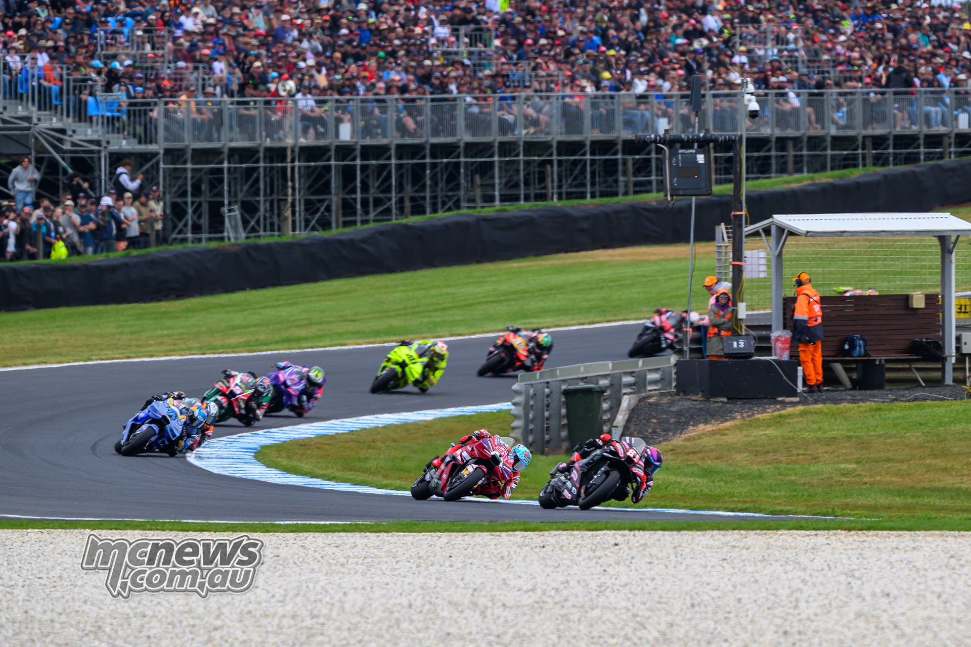Jorge Martin leads Marc Marquez through a corner, with Alex Marquez and a line of riders following in front of a packed grandstand.