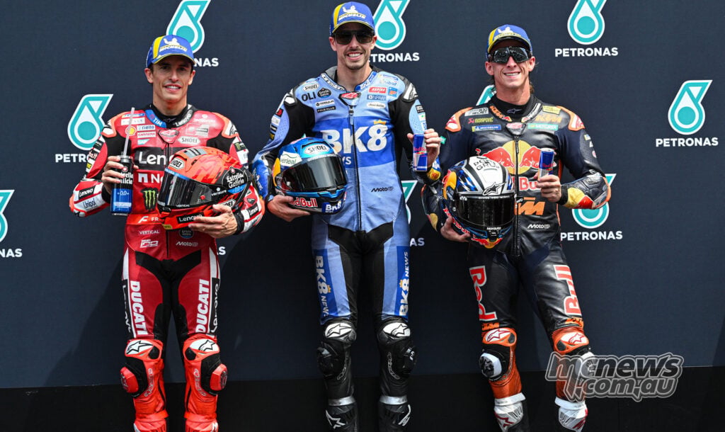 Alex Marquez in blue Gresini Ducati leathers stands between Marc Marquez in red Ducati leathers and Pedro Acosta in black and orange KTM leathers following Malaysian MotoGP qualifying at Sepang.