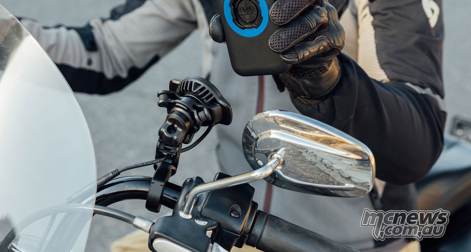 Motorcyclist wearing black riding gloves holding a smartphone fitted with a Quad Lock case above the adjustable motorcycle handlebar mount